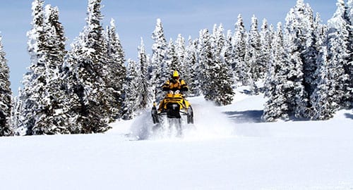 Yellow snowmobile riding through fresh powder snow.