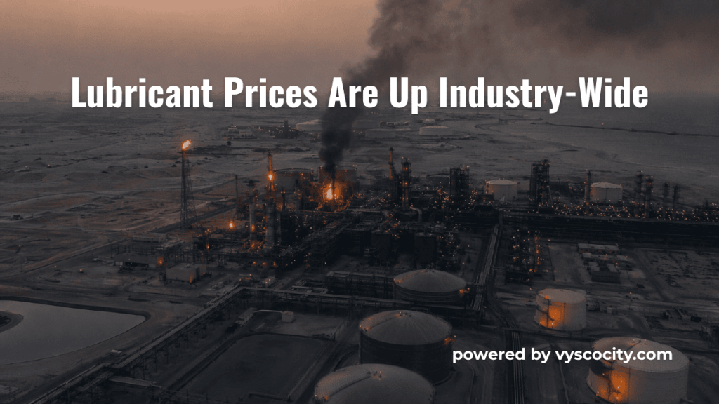 Aerial view of a petroleum refinery complex at dusk with black smoke rising from a processing unit, representing the global supply chain disruption driving industry-wide lubricant price increases in 2026