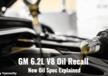 Close-up of motor oil being poured into a GM 6.2L V8 engine with overlay text about an oil recall and new specification update.